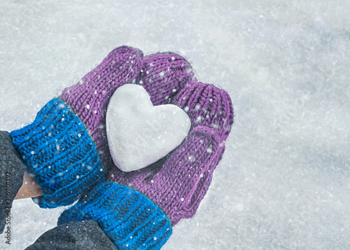 Female hands in knitted mittens with heart of snow in winter day. Love concept. Valentine day background.