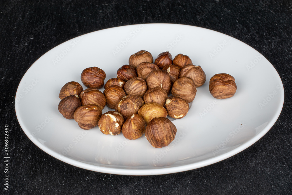 Lot of whole tasty brown hazelnut on white ceramic plate on grey stone Lot of whole tasty brown hazelnut on white ceramic plate on grey stone