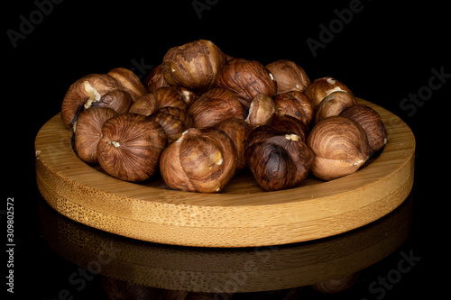 Lot of whole tasty brown hazelnut on round bamboo coaster isolated on black glass