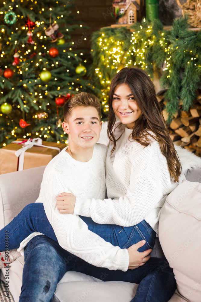 young beautiful couple sitting in a beautiful room on the bed against the background of the Christmas tree and smiling