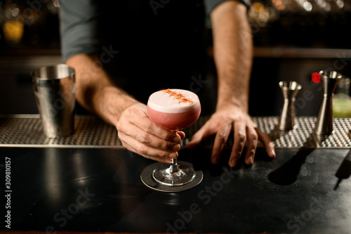 Bartender holding decorated alcohol cocktail in small glass