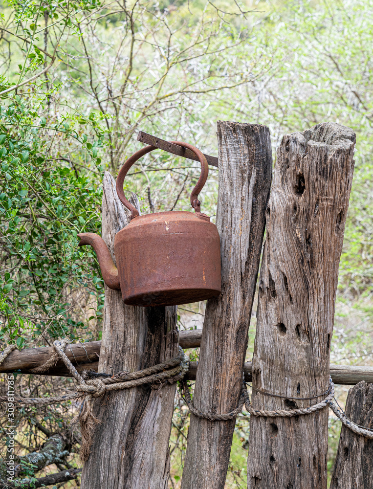 Fototapeta premium Rostiger Wasserkessel hängend am Holzzaun