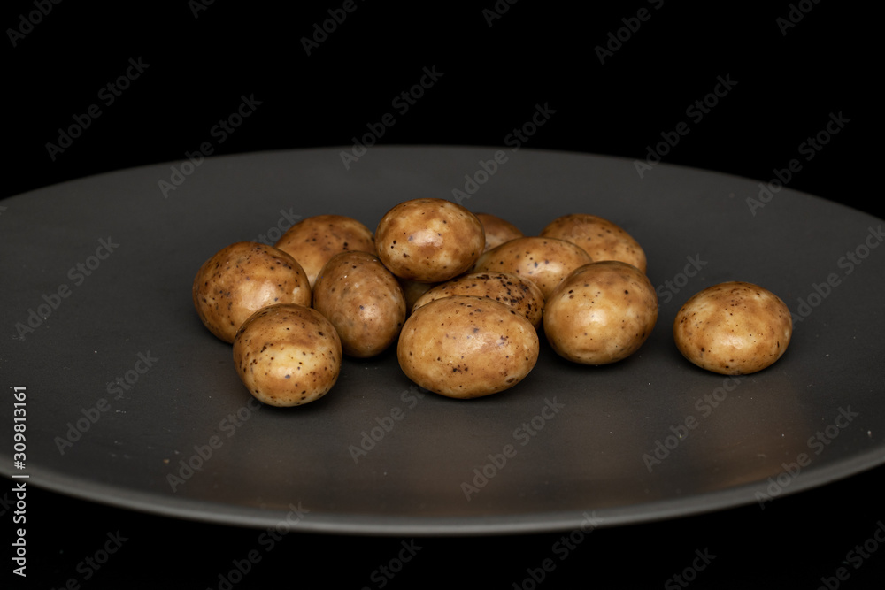 Lot of whole tiramisu brown almond nut on gray ceramic plate isolated on black glass