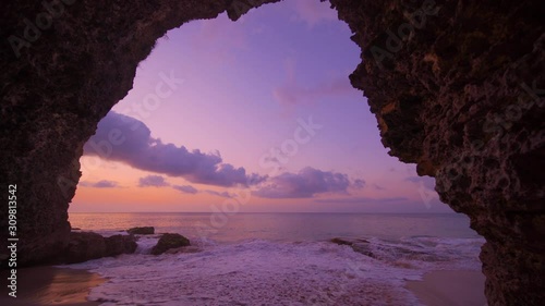 View from the cave a sandy beach along the ocean at golden sunset. Bali, Indonesia.