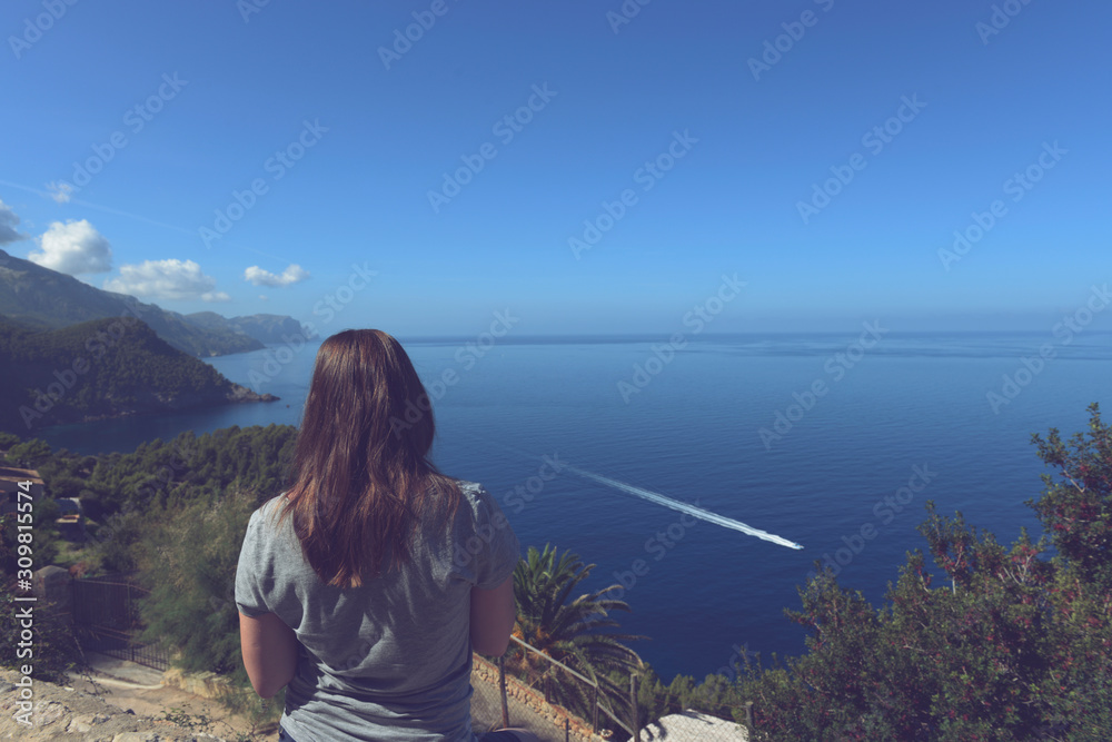 Back view of a young tourist woman looking at the ocean from the cliff