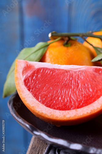 Slices of red grapefruit and whole mandarins with green leaves on the black plate