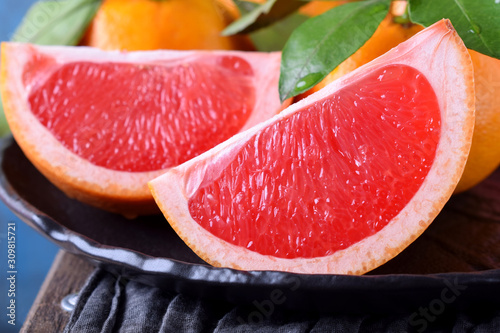 Slices of red grapefruit and whole mandarins with green leaves on the black plate