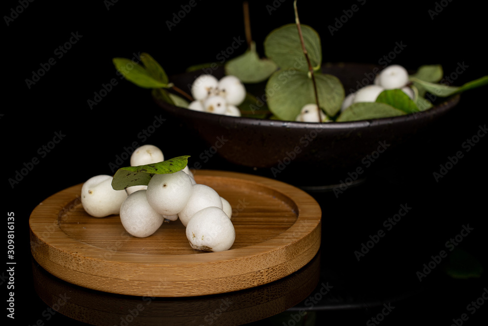Lot of whole white snowberry on round bamboo coaster in glazed bowl isolated on black glass Lot of whole white snowberry on round bamboo coaster in glazed bowl isolated on black glass