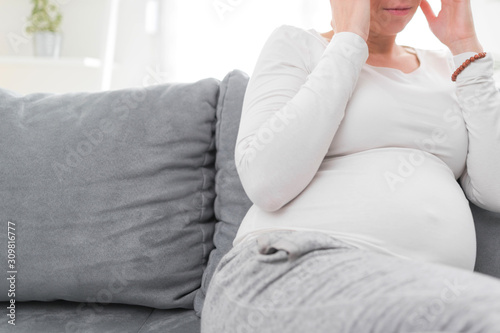 Pregnant tired exhausted woman with stomach and head issues at home on a couch, being sick.