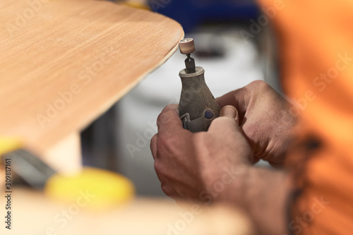 Detail of carpenter's hands filing the edge of a wooden plank with a Dremel tool. Top view photo