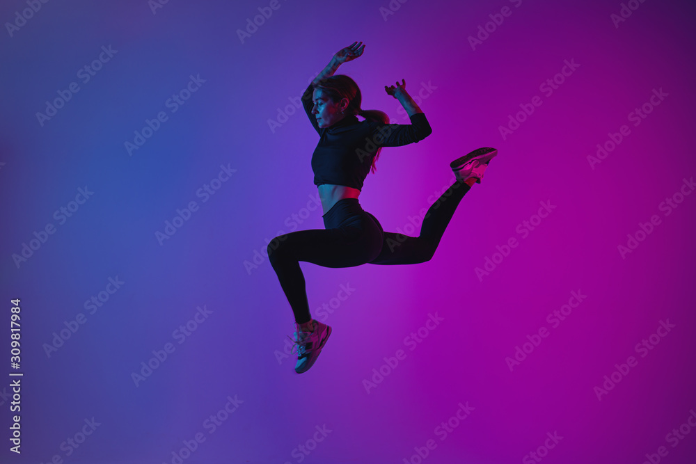 Fit sporty woman jumping in studio against phantom blue color background. Young beautiful girl in jumping moment