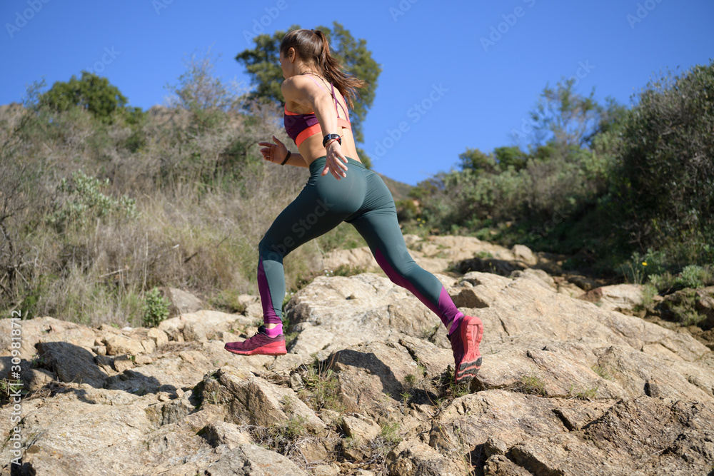 Naklejka premium Sportswoman runs up a rock-filled mountain trail while doing her daily workout