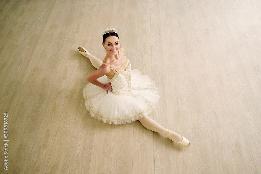 Naklejka premium Top view of cheerful graceful ballerina sitting with legs stretched out in the ballet studio
