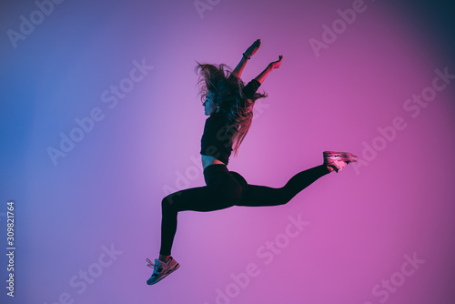 Fototapeta Naklejka Na Ścianę i Meble -  Fit sporty woman jumping in studio against phantom blue color background. Young handsome girl in jumping moment