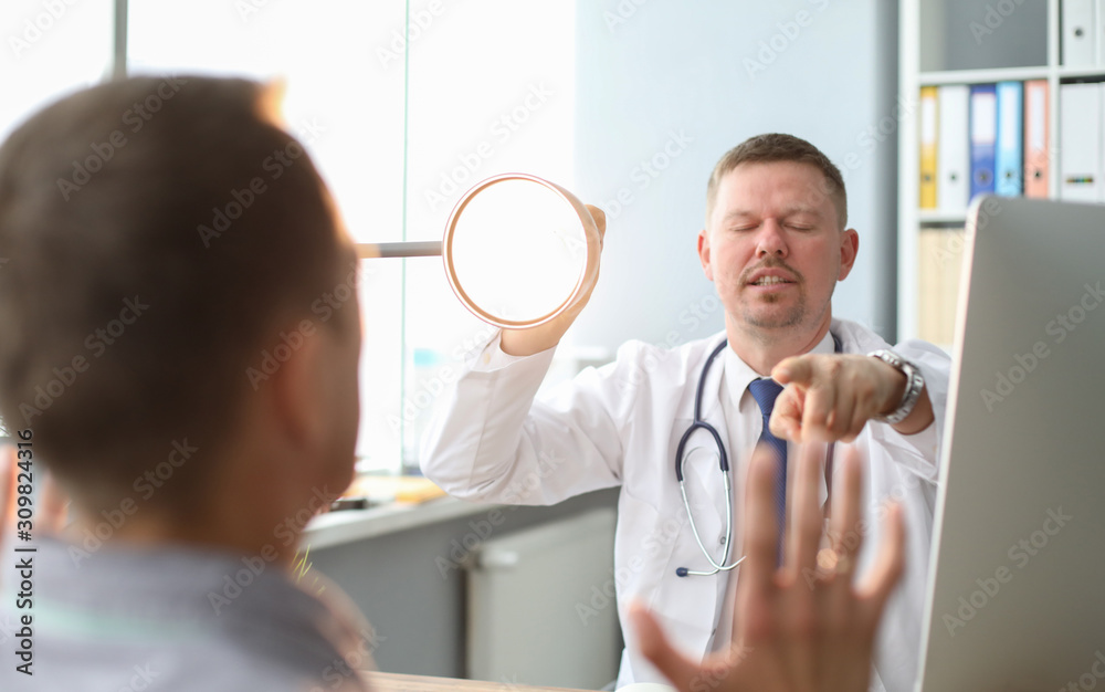 Angry doctor interrogates the patient, yelling at him, pointing to man he talking to and holding lamp base. Angry doctor interrogates the patient, yelling at him, pointing to man he talking to and holding lamp base.