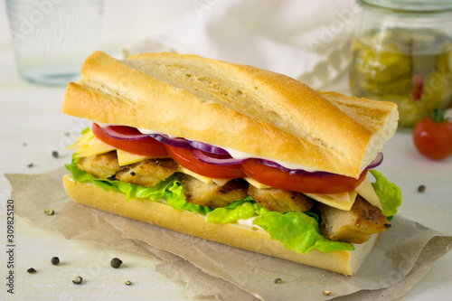 Food photography of a grilled chicken sandwich with tomatoes and red onions on a baguette bread on a white background