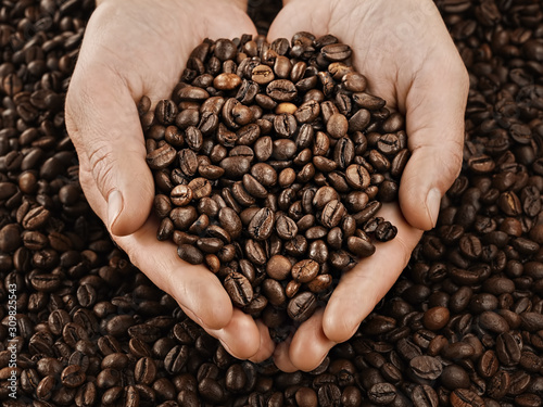 Roasted coffee beans in female hands  background. Horizontal orientation. Fresh aromatic dark coffee. Close-up. Selective focus on hands with coffee beans.