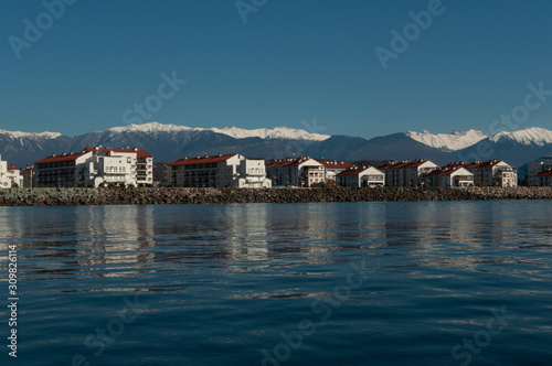 a number of typical four-story houses near the sea. Mountain snow-capped peaks rise above the roofs of houses © Alexei Merinov