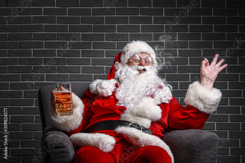 Funny drunk Santa Claus showing OK while sitting in armchair against brick background