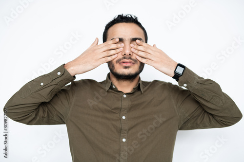 Young tired man in shirt covering his eyes by hands at break between work