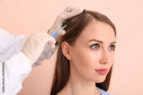 Woman with hair loss problem receiving injection on color background