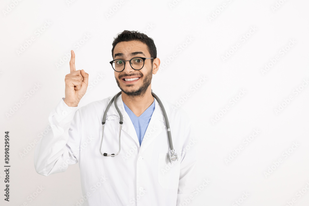 Young smiling therapeutist in whitecoat and eyeglasses pointing upwards