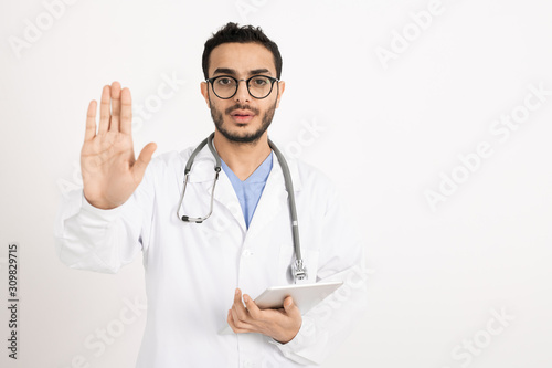 Young practitioner in whitecoat and eyeglasses showing warning sign by hand