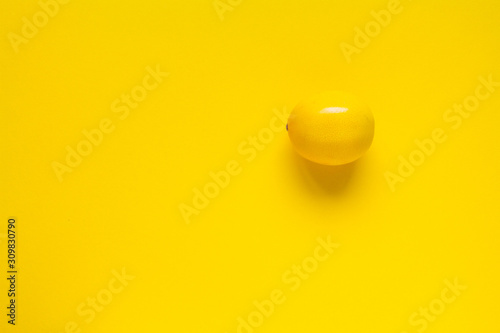 Ripe yellow lemon on a yellow surface, minimalistic background or concept