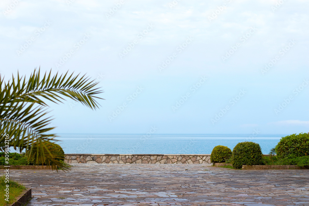 Embankment by the sea with palm trees. Natural stone pavement with blue sea and blue sky. Tourism and vacation.
