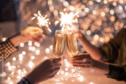 Hands of couple with flutes of champagne and their friends with bengal lights photo