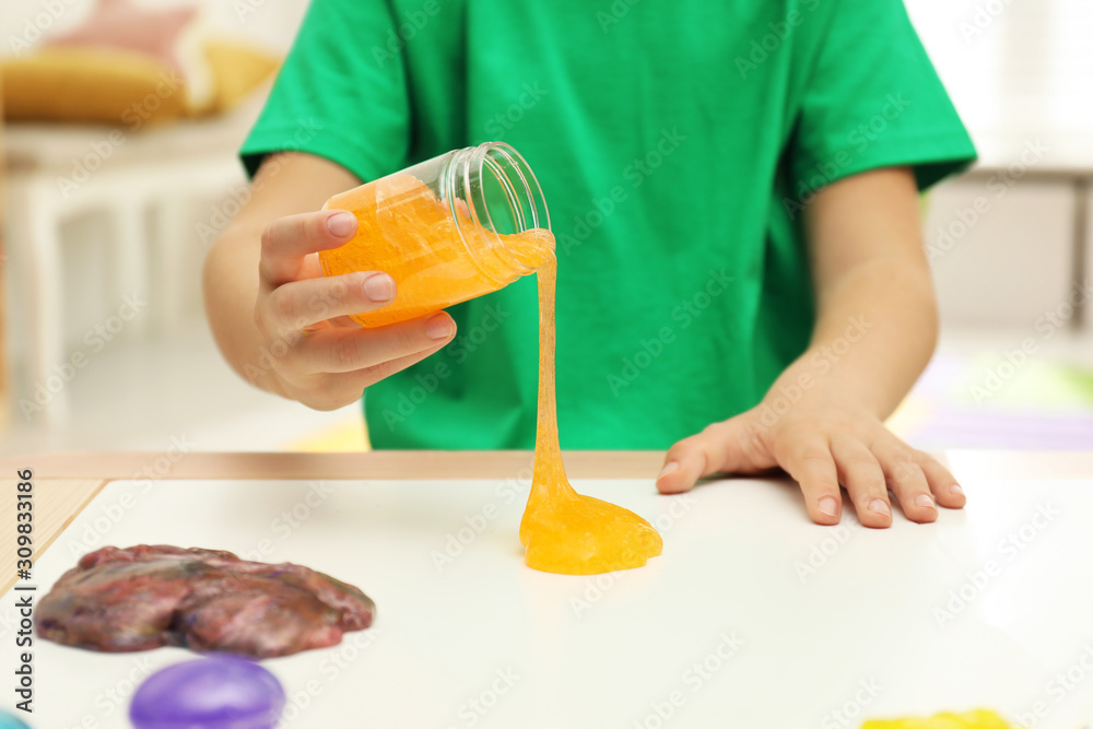 Little boy pouring slime onto table indoors, closeup