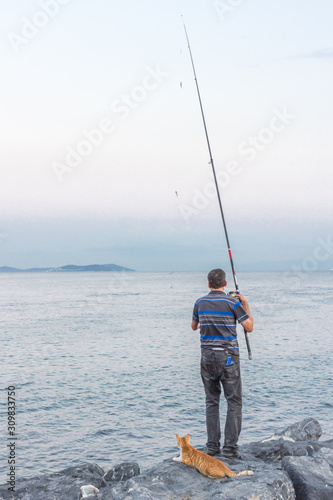 Fisherman on the seashore. Fishing on the Bosphorus. Friendship between man and animal. Man and cat. Fisherman with fishing rod for fishing. Cat waiting for a fish catch. Joint activity.