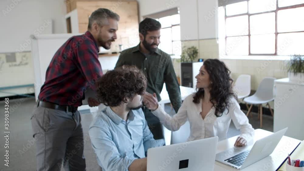 Handsome bearded man walking to cheerful colleagues and shaking hands. Group of young people working together in cozy office. Startup concept Handsome bearded man walking to cheerful colleagues and shaking hands. Group of young people working together in cozy office. Startup concept