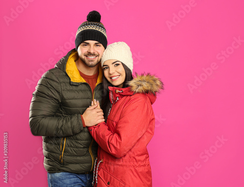 Happy young couple in warm clothes on pink background, space for text. Winter vacation