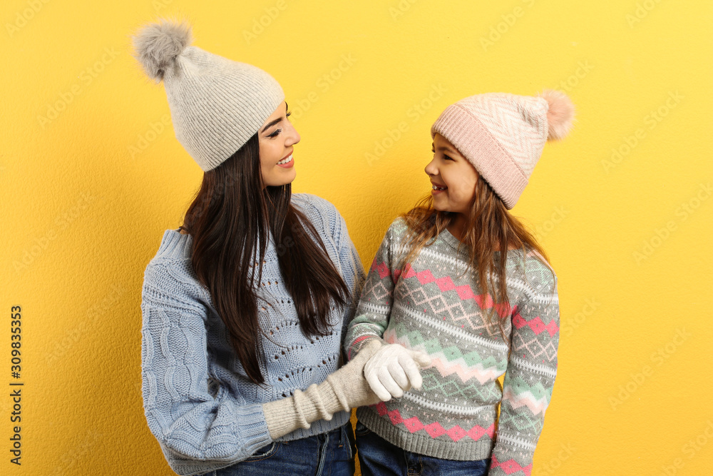 Happy mother and daughter in warm clothes on yellow background. Winter vacation Happy mother and daughter in warm clothes on yellow background. Winter vacation