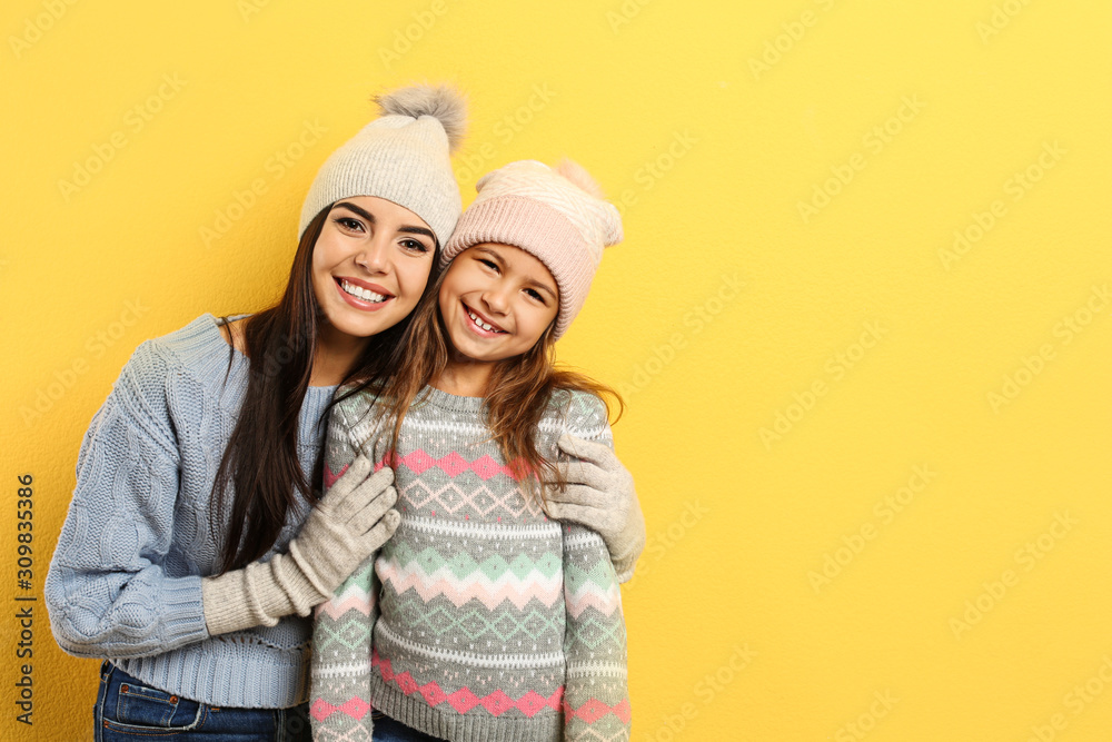 Happy mother and daughter in warm clothes on yellow background, space for text. Winter vacation Happy mother and daughter in warm clothes on yellow background, space for text. Winter vacation
