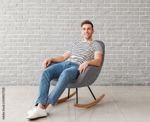 Handsome man sitting in armchair near brick wall © Pixel-Shot