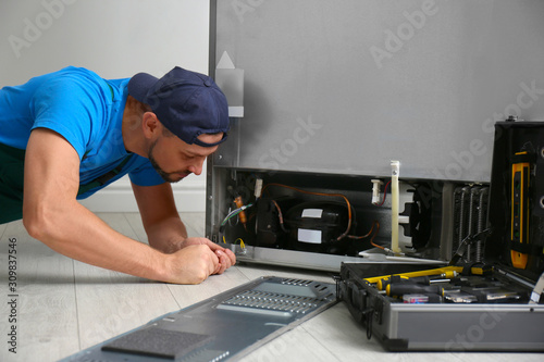 Male technician with screwdriver repairing refrigerator indoors
