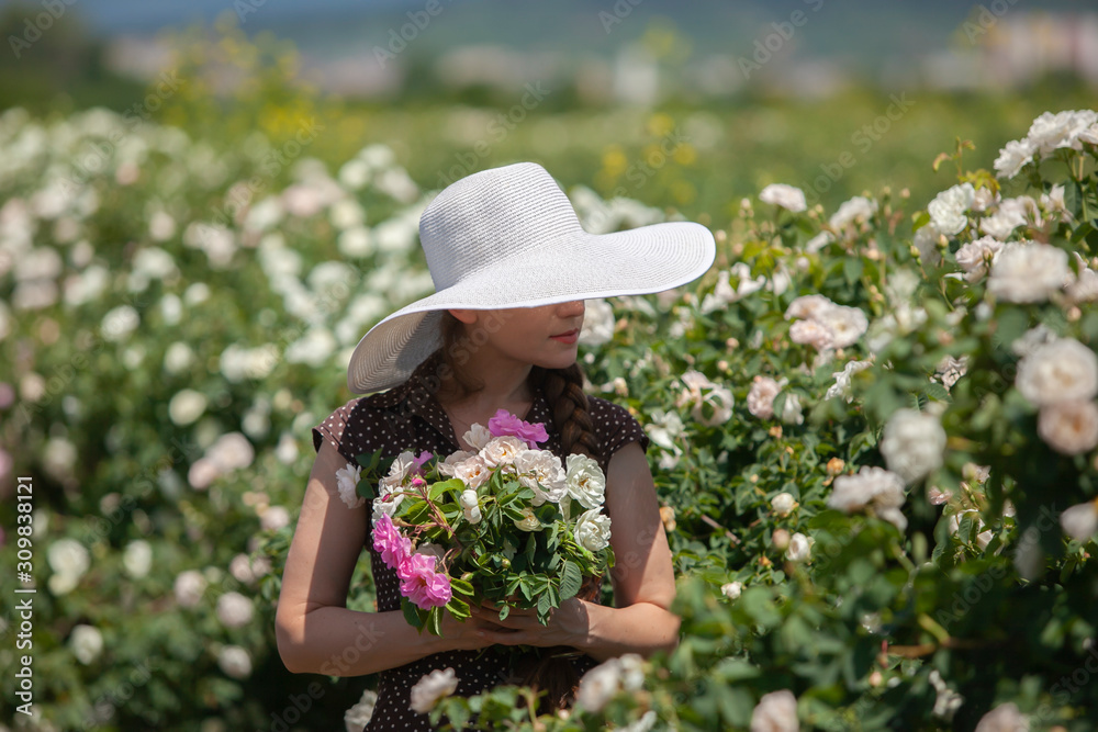 Beautiful woman in retro style polka dot dress and hat holding a delicate bouquet of Bulgarian pink fresh roses