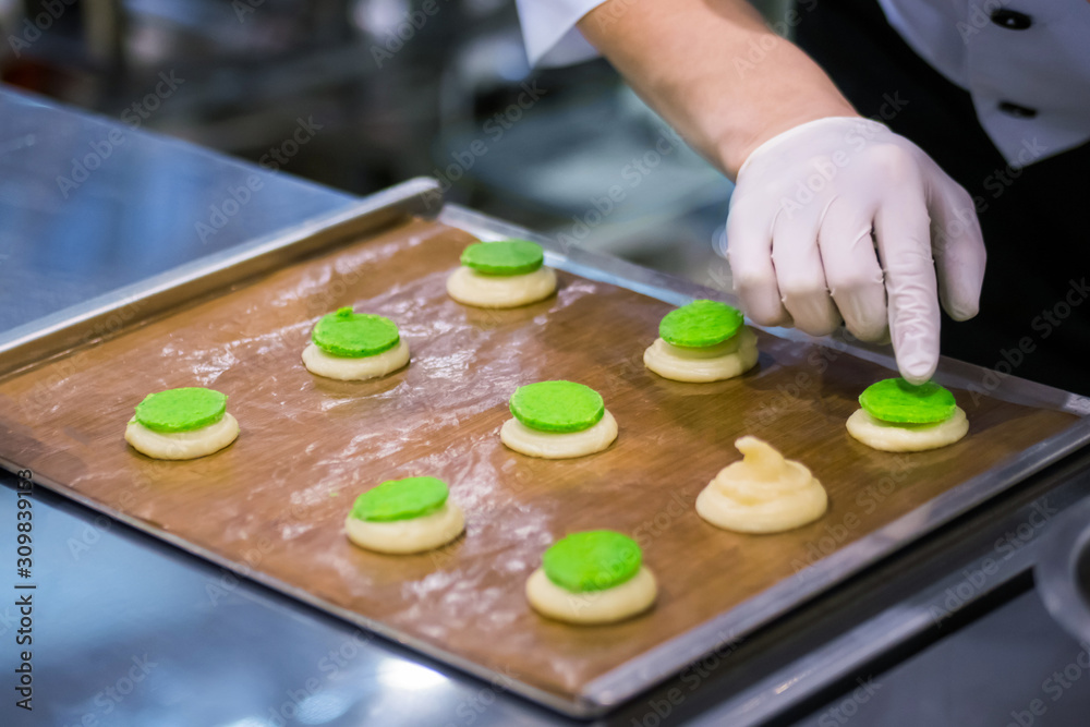 Process of preparing shortbread cookies with bright green filling on kitchen table at cuisine of bakery, restaurant. Professional cooking, catering, bakery, gastronomy and food concept