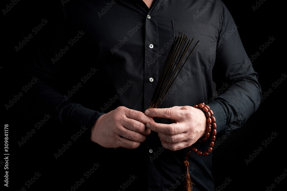 adult man in black clothes holds a stack of incense stick