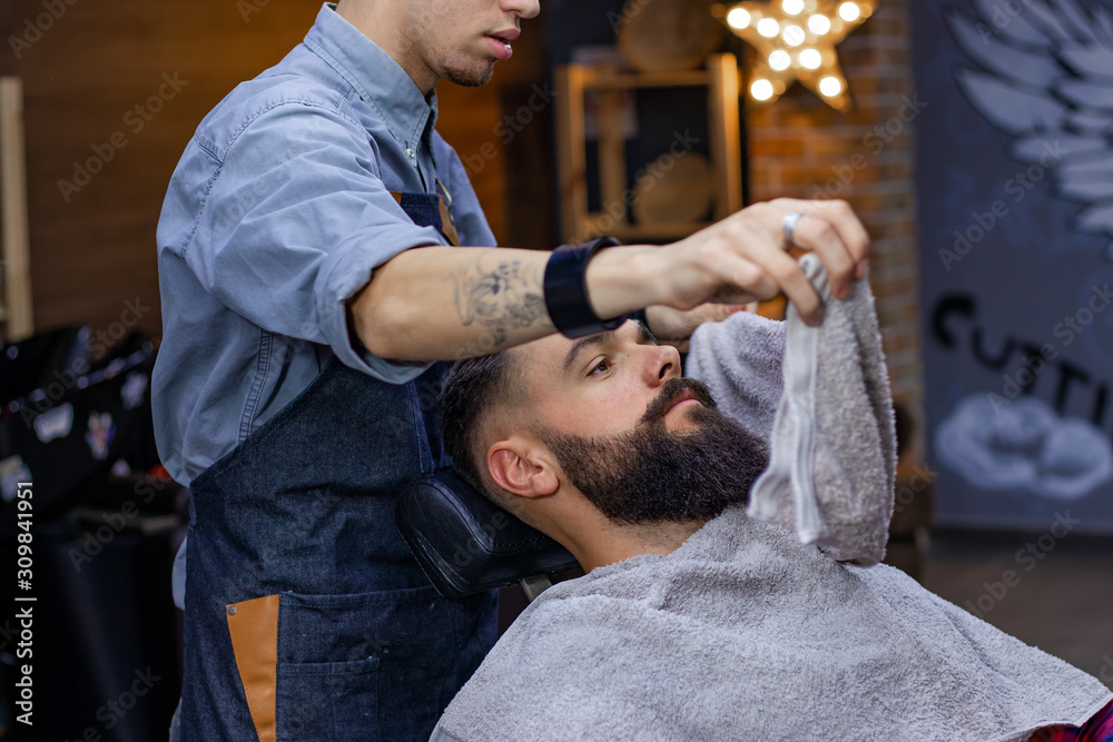 Barber covers the face of a young bearded man with a hot towel before  shaving at barbershop. Advertising and barber shop concept. Stock-Foto |  Adobe Stock