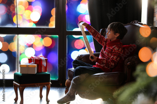Little boy with wish list to Santa Claus near window indoors. Christmas holiday