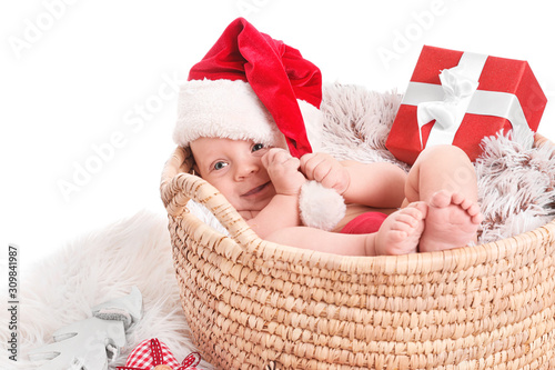 Cute little baby with Santa Claus hat and Christmas gift lying in basket on white background