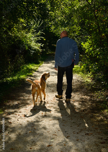 Man talking to his dog while on a walk on a path in a green forest of Toronto