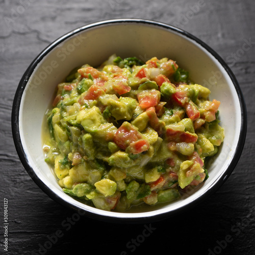 Mexican guacamole with tomato on dark background