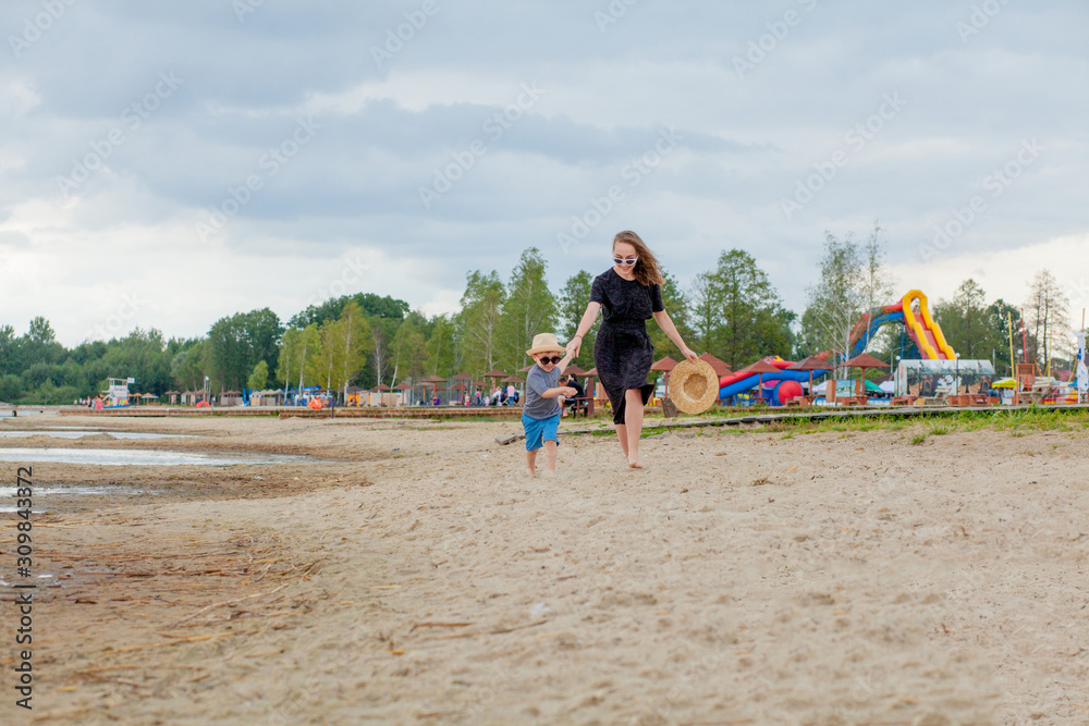 A young beautiful girl runs along a sandy beach in the sea with her son A young beautiful girl runs along a sandy beach in the sea with her son