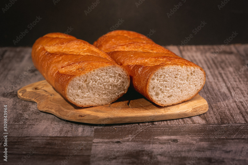 There are two Golden toasted crispy mouthwatering freshly baked baguette halves lying on a wooden Board. White bread