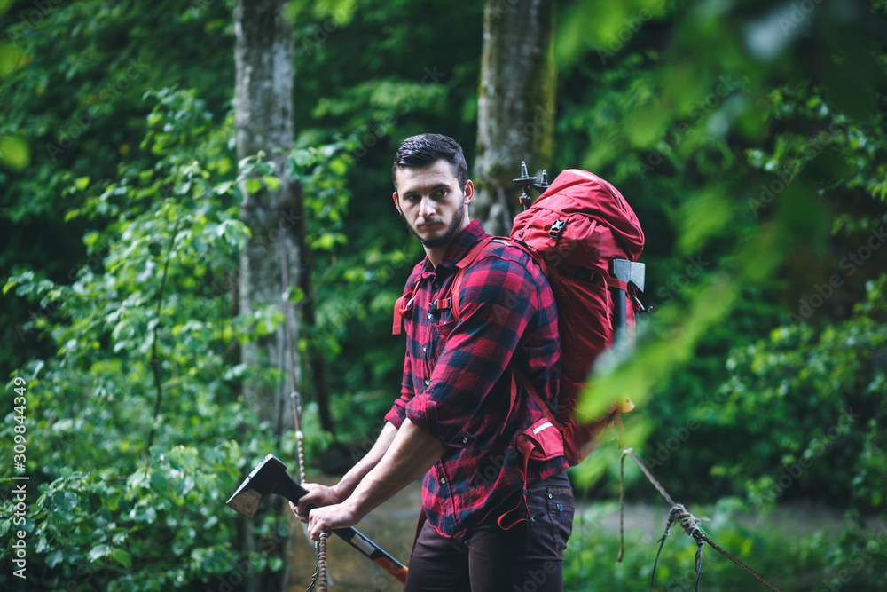 Handsome Man in a Plaid Shirt goes through the Woods with an Axe