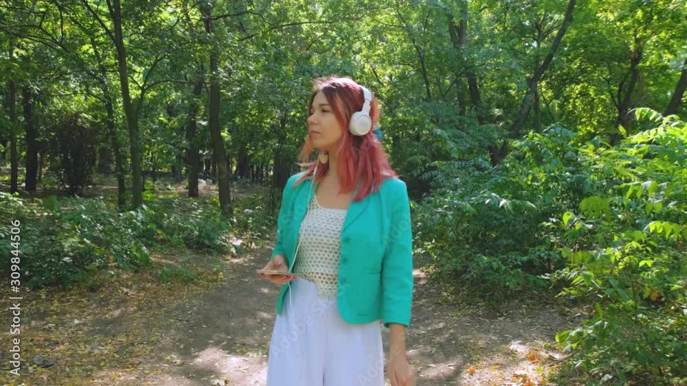 Young happy woman in colorful suit and with pink hair walk in summer park and listen to music Young happy woman in colorful suit and with pink hair walk in summer park and listen to music